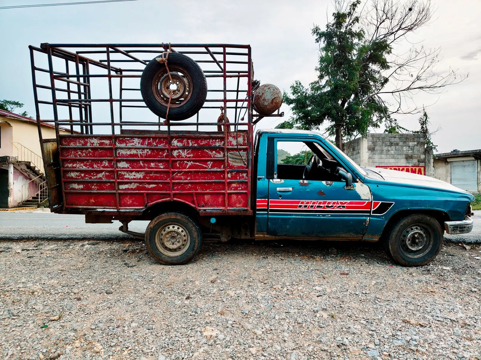 Old blue and red pickup truck with a metal cage parked on a gravel road.